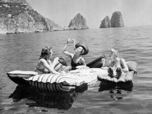 Pasta Picnic at Sea, pasta, spaghetti, women, women eating pasta, floating picnic, inflatable raft, black and white photography, vintage photography, beach scene, seaside, ocean, sea, Mediterranean, Capri, Italy, summer, vacation, travel photography, retro lifestyle, leisure, carefree, playful, candid photography, friends, female friendship, swimsuit, sun hat, floating lunch, food photography, travel art, coastal decor, resort life, glamorous, mid century, vintage travel, iconic photography, summer fun, storytelling, monochrome, black and white, lifestyle photography, conversation piece, European travel, nostalgic, joyful, vacation vibes, art photography, wall art, seaside escape, women at leisure, retro charm, coastal lifestyle, sunny day, famous photograph