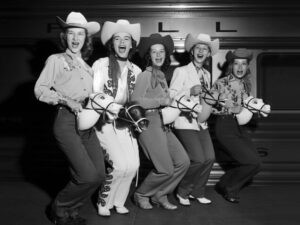 Cowgirls Riding Stick Horses, cowgirls, stick horse, cowboy hats, western, vintage photograph, black and white, americana, playful, group portrait, rodeo, retro, ranch, old west, costume