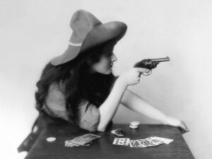 Cowgirl Playing Cards With Revolver, cowgirl, revolver, playing cards, cowboy hat, western, vintage photograph, black and white, gambler, old west, americana, portrait, frontier, saloon, dramatic